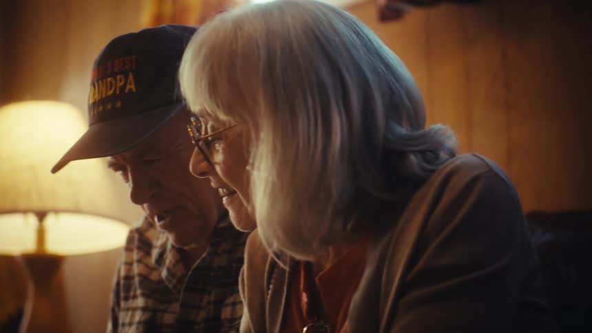 An elderly couple smiles warmly while reminiscing over old memories together in their sunlit living room