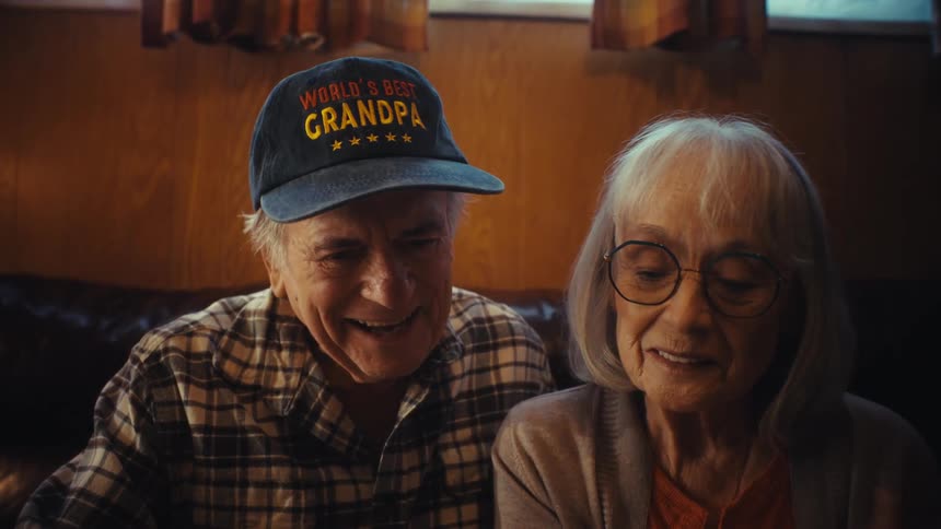 An elderly couple reminisces with joy and nostalgia as they look through an old family photo album together on their couch