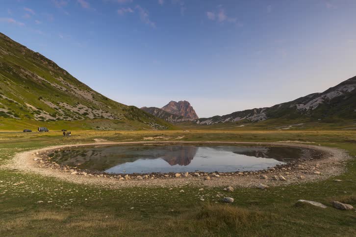 A stunning timelapse captures the sunrise over a tranquil mountain valley, with the peak reflecting in a still pond as golden light illuminates the landscape