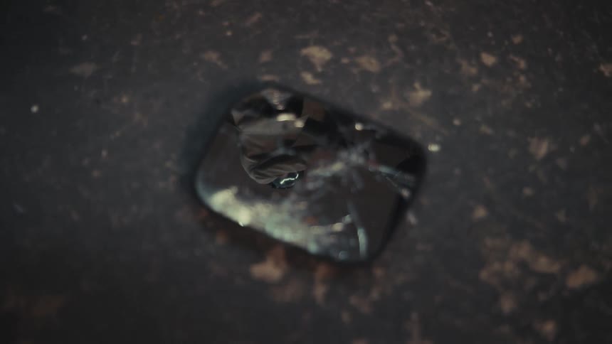 Small pieces of glass fall in slow motion onto a shattered smartphone screen on a dark surface