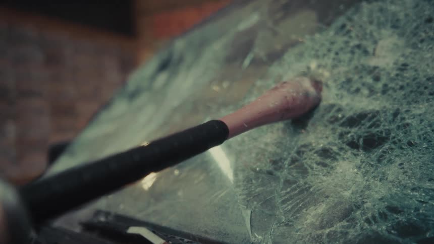 A slow camera pull back reveals a baseball bat smashed through the shattered windshield of a dusty, old car