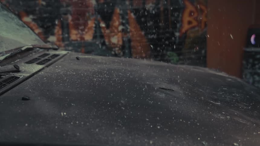 Slow motion shot of a crowbar smashing into a dusty car hood, sending debris flying into the air