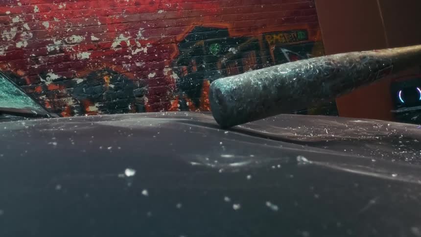 Super slow-motion of a baseball bat smashing the hood of a car in a gritty urban alley