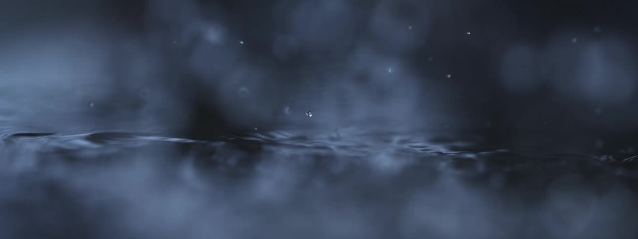 Atmospheric slow-motion macro view of raindrops falling into dark water, creating beautiful ripples and bokeh