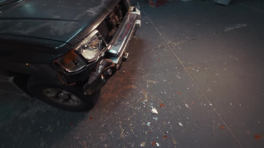 A first-person view of someone aggressively smashing a damaged car's headlight with a baseball bat in a dark garage