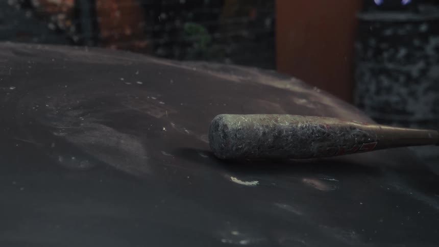 A dirty baseball bat drops onto a dusty surface and is picked up in super slow motion