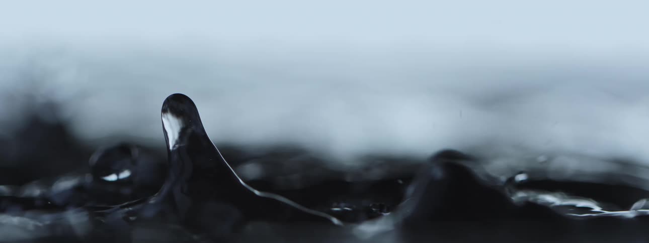 A moody, super slow-motion macro shot of water droplets splashing and bouncing on a liquid surface