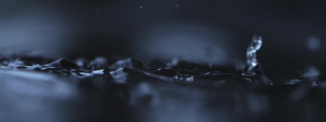 A dramatic close-up of water droplets splashing onto a dark surface in mesmerizing slow motion