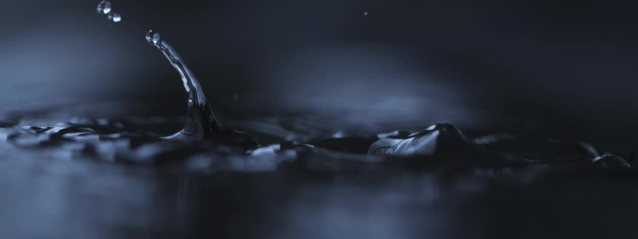 An elegant super slow-motion macro shot of water droplets creating ripples and splashes on a dark surface