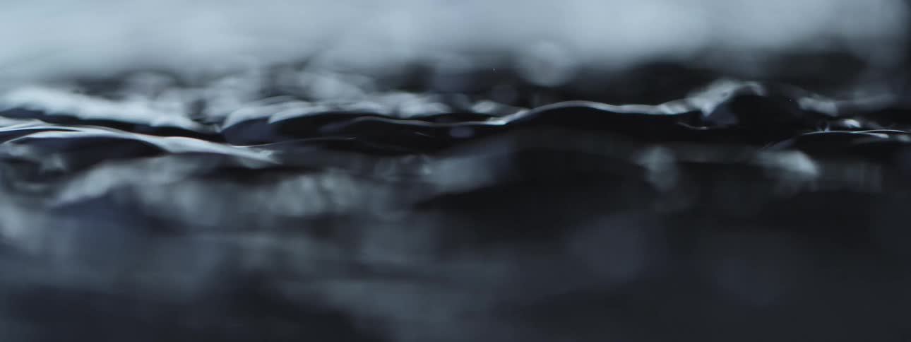A dramatic slow-motion macro shot of a water drop impacting a dark, calm surface and creating ripples