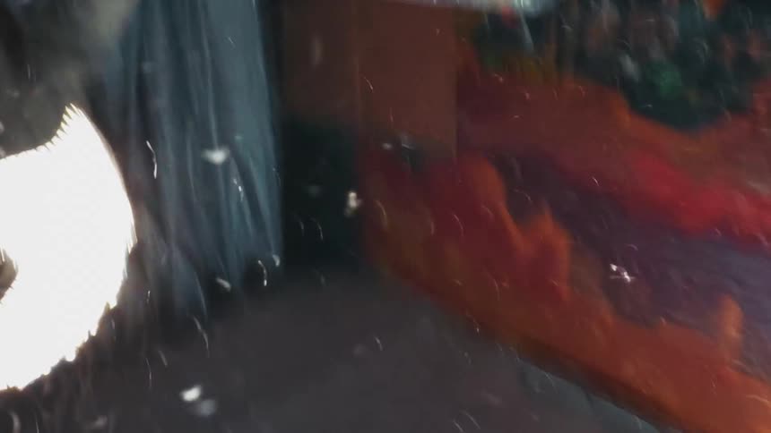 Chaotic slow-motion reflection of a person hitting something with a baseball bat, causing an explosion of feathers in a gritty urban setting