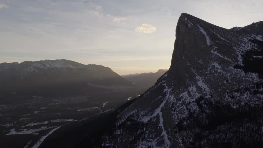 A static aerial view of a majestic, snow-covered mountain peak silhouetted against the hazy morning sunrise