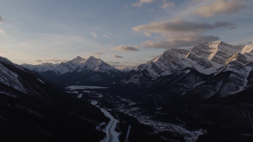 Majestic snow-capped mountains tower over a vast valley and a frozen winding river during a serene winter sunrise