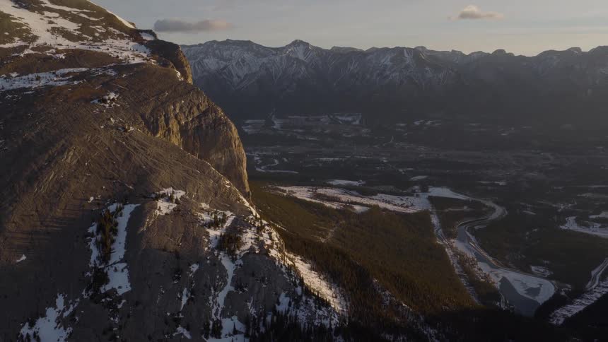 A majestic aerial view reveals a vast, snowy mountain landscape and a river valley basking in the golden light of sunrise