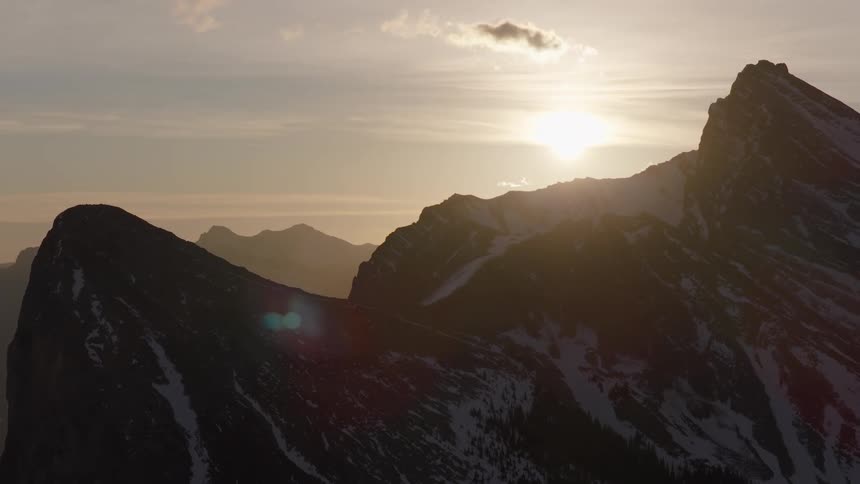 An epic aerial shot reveals a vast, snowy mountain range silhouetted by the golden setting sun