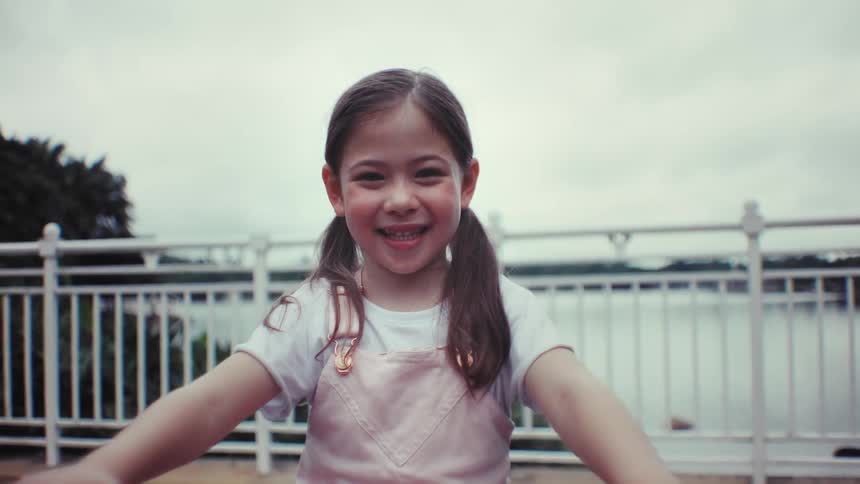 Portrait of a joyful young girl with pigtails smiling brightly in front of a lake