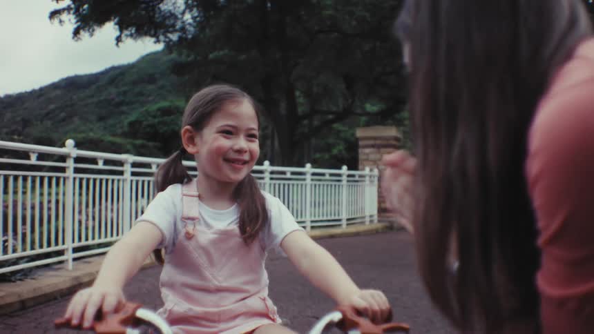 An adorable little girl happily rides her bike towards her mother and they share a loving hug in the park