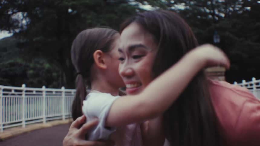 An adorable little girl happily rides her bike towards her mother and they share a loving hug in the park