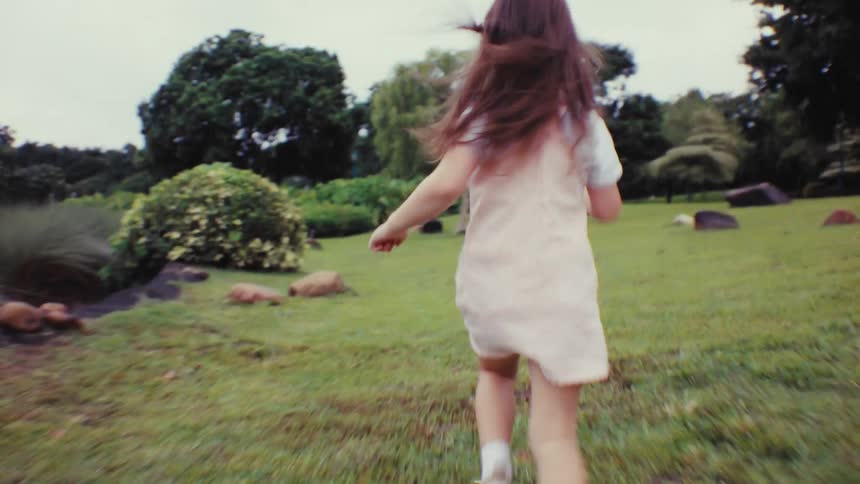 A carefree young girl runs in slow motion through a beautiful green park in this dreamy, vintage-style clip