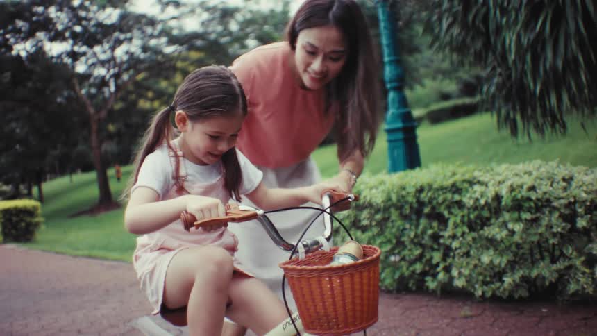 A happy mother teaches her young daughter how to ride a bicycle for the first time in a beautiful green park