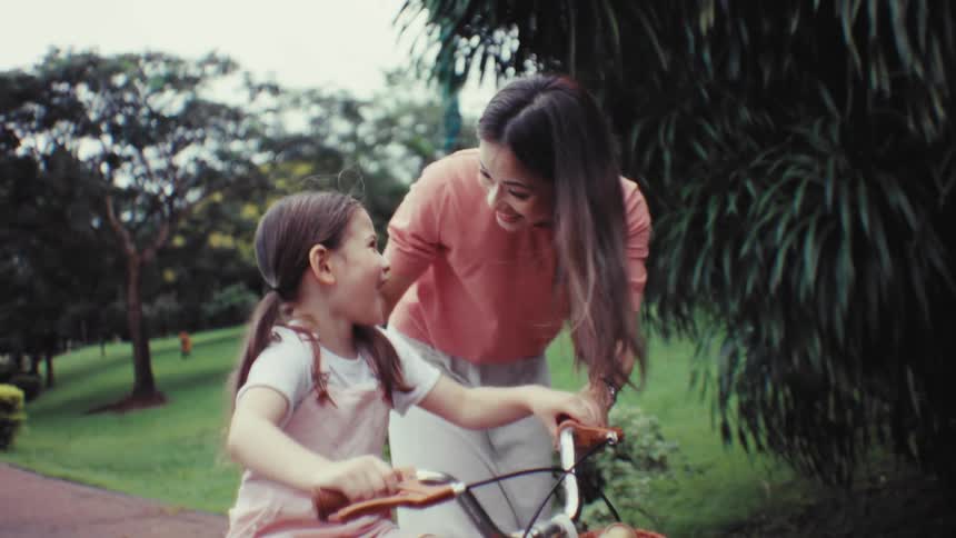 A happy mother teaches her young daughter how to ride a bicycle for the first time in a beautiful green park
