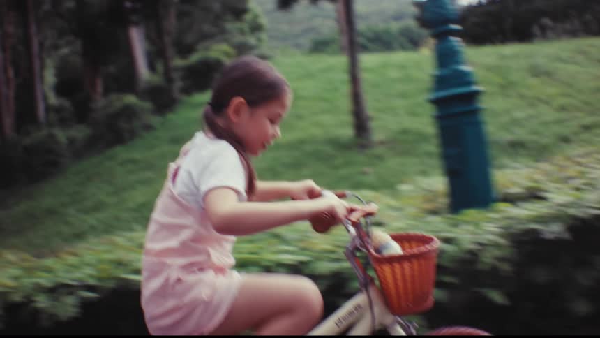 A mother teaches her young daughter to ride a bicycle in the park, letting go as the happy girl rides on her own for the first time