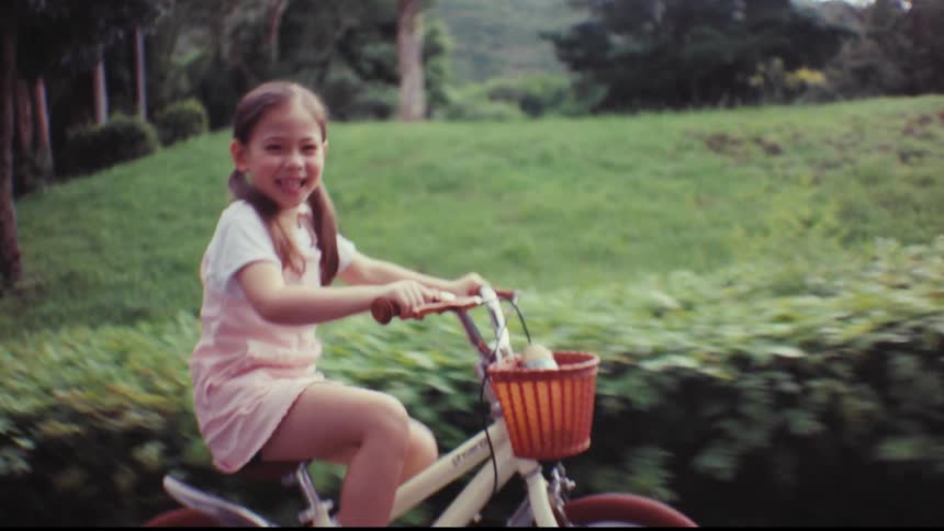 A mother teaches her young daughter to ride a bicycle in the park, letting go as the happy girl rides on her own for the first time