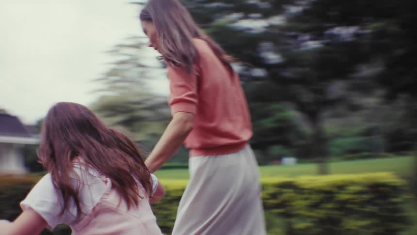 A caring mother teaches her happy young daughter how to ride a bicycle with training wheels along a scenic park path