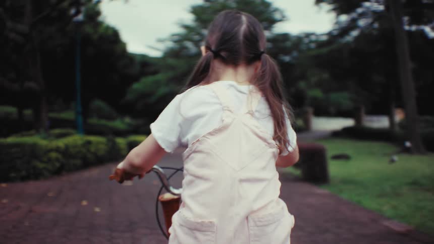 A mother teaches her happy daughter to ride a bike in a lakeside park, then watches her ride off on her own