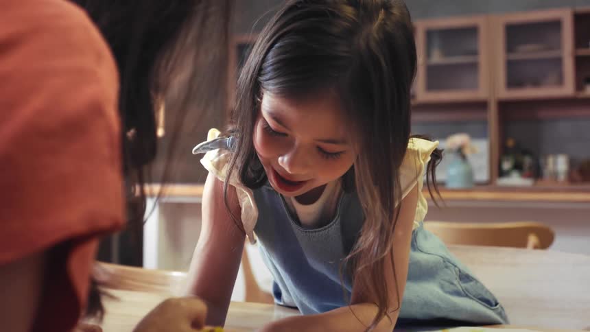 A loving mother and her happy young daughter spend quality time together drawing with crayons at their kitchen table