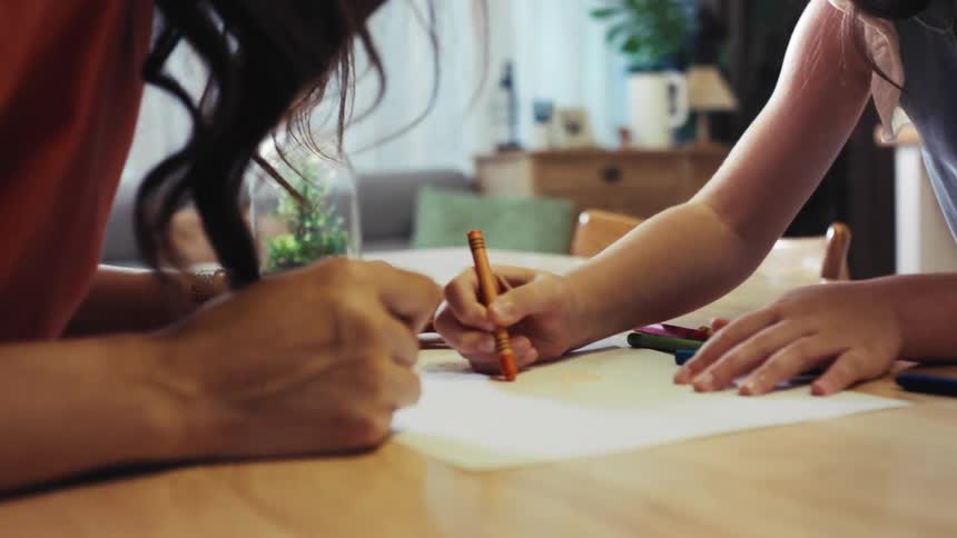 A young girl joyfully claps after finishing a drawing with her mother at home