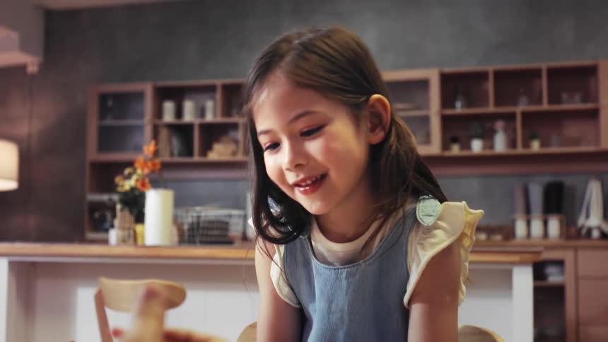 An adorable little girl's face lights up with a joyous smile as she draws with her mother in their modern kitchen