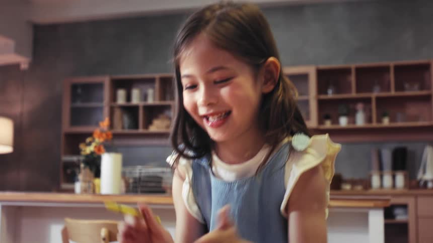 An adorable little girl's face lights up with a joyous smile as she draws with her mother in their modern kitchen