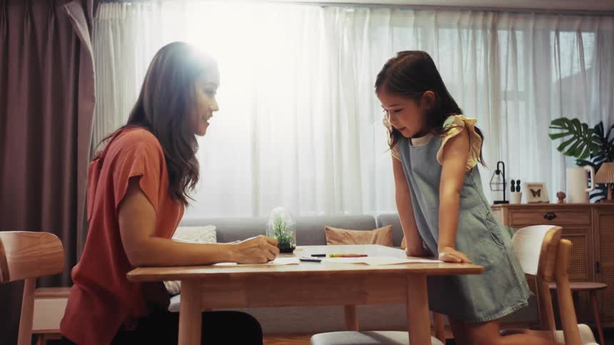 Happy Asian mother and her adorable daughter have a creative drawing session, ending with a joyful high-five in their cozy living room
