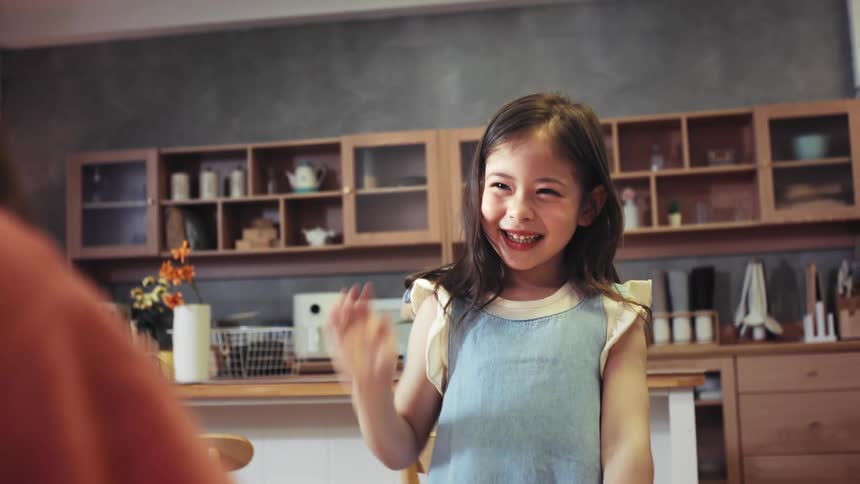A delighted little girl with a huge smile gives her mother a high-five in slow motion in their modern kitchen