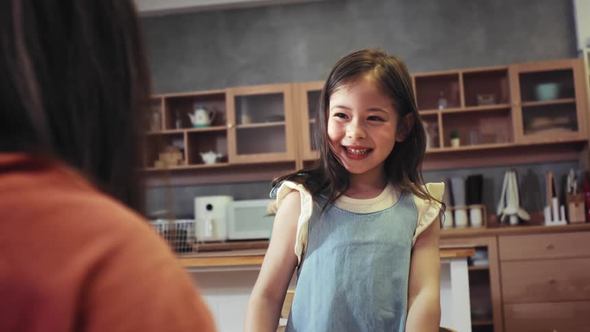 A delighted little girl with a huge smile gives her mother a high-five in slow motion in their modern kitchen