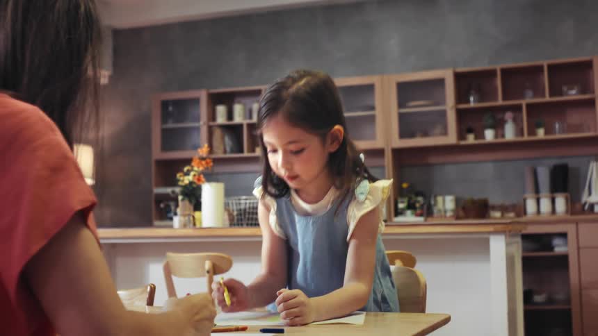 A young girl joyfully claps and cheers while coloring with her mother at the kitchen table in slow motion