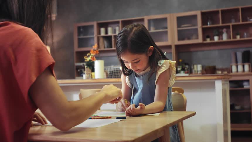 A young girl joyfully claps and cheers while coloring with her mother at the kitchen table in slow motion