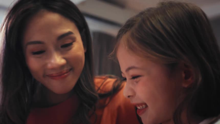 A loving Asian mother and her cute daughter share a happy moment drawing and coloring together in their living room