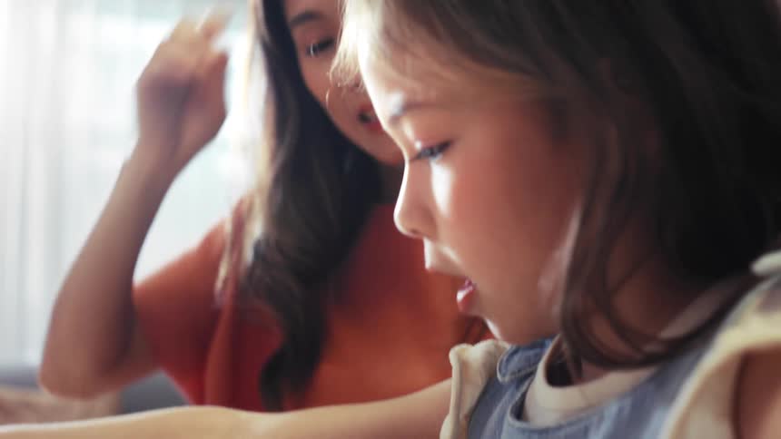 A loving Asian mother and her cute daughter share a happy moment drawing and coloring together in their living room