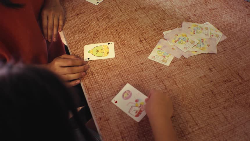 An over-the-shoulder view of a mother and child playing a fun cartoon card game at the kitchen table