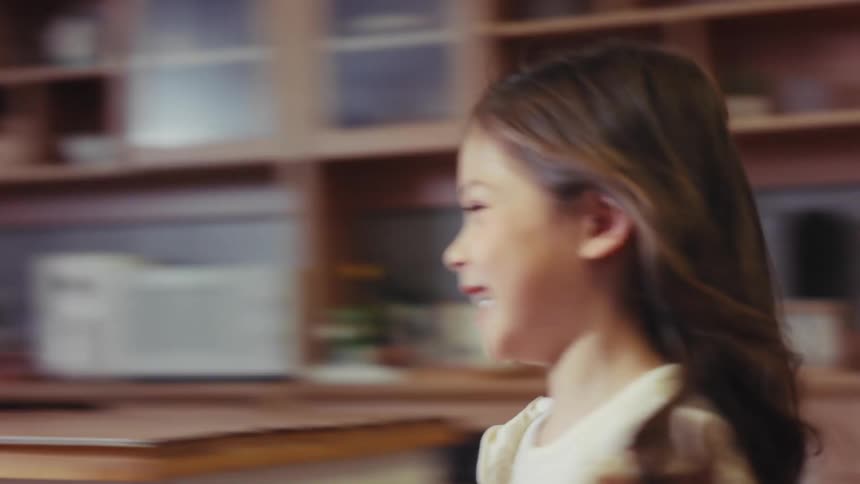 Slow motion footage shows a happy little girl with long hair running joyfully through the house and jumping on the sofa