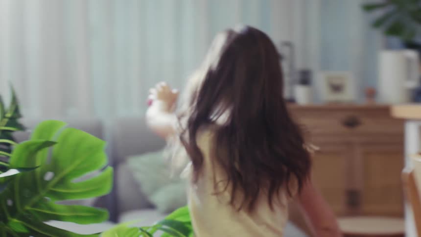 Slow motion footage shows a happy little girl with long hair running joyfully through the house and jumping on the sofa