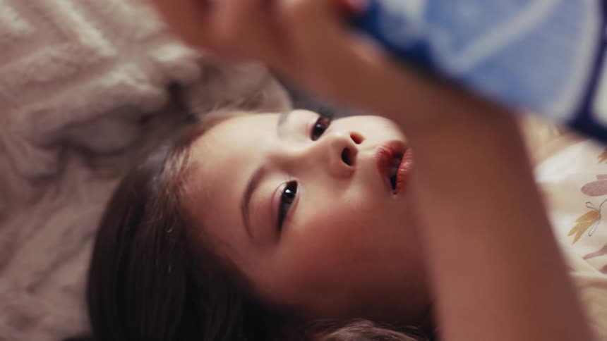 An intimate close-up of a young girl's face as she lies in bed and reads a captivating storybook