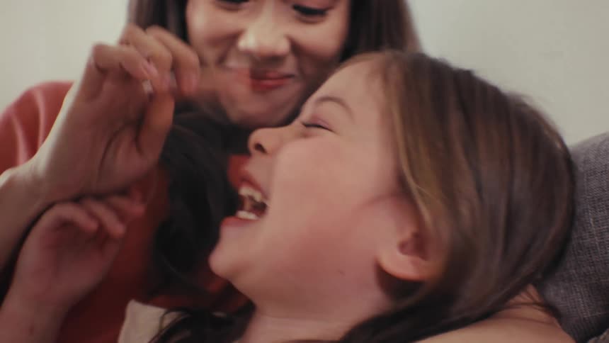 A joyful young girl laughs hysterically in slow motion while her mother playfully teases her in a loving moment at home