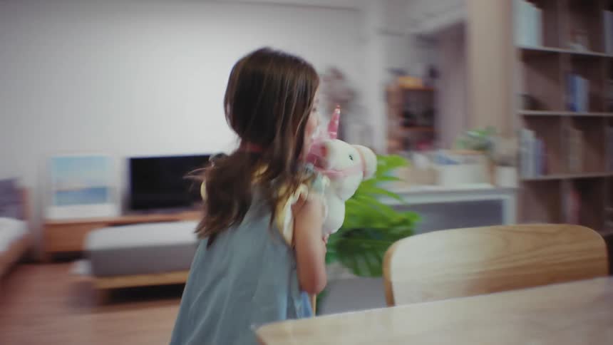 A joyful little girl in a blue dress runs energetically through her home, happily playing with her unicorn hobby horse