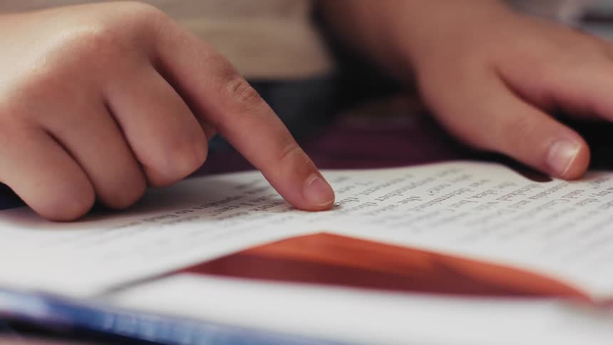 Close up of a young child's finger pointing at words on a page as they learn to read