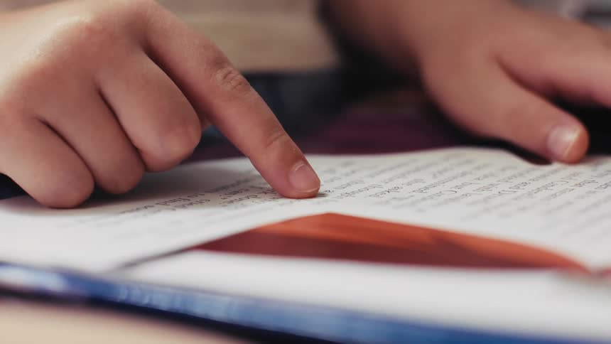 Close up of a young child's finger pointing at words on a page as they learn to read