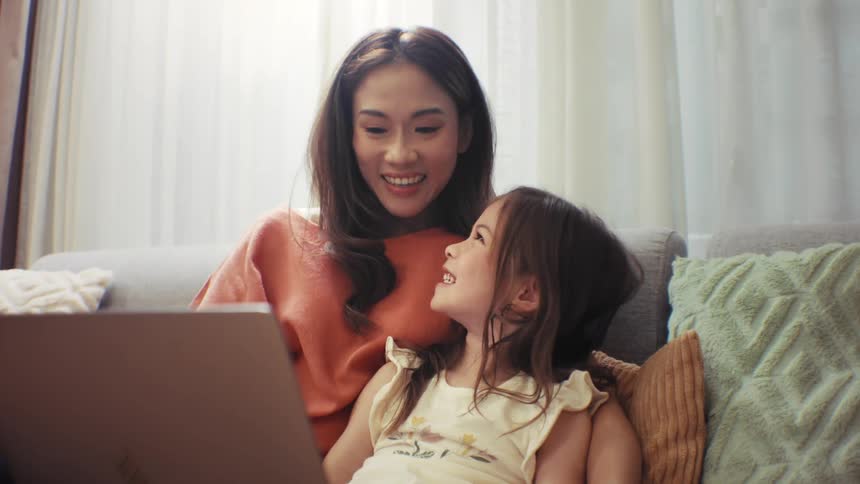 A heartwarming slow-motion shot shows a loving mother and her daughter sharing a happy moment while looking at a laptop at home