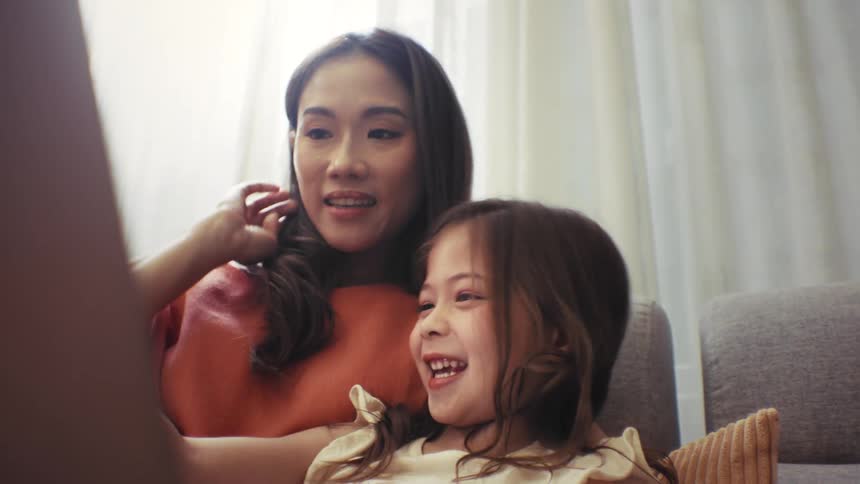 Loving mother and her happy daughter share a joyful moment hugging and watching a laptop together on the sofa at home